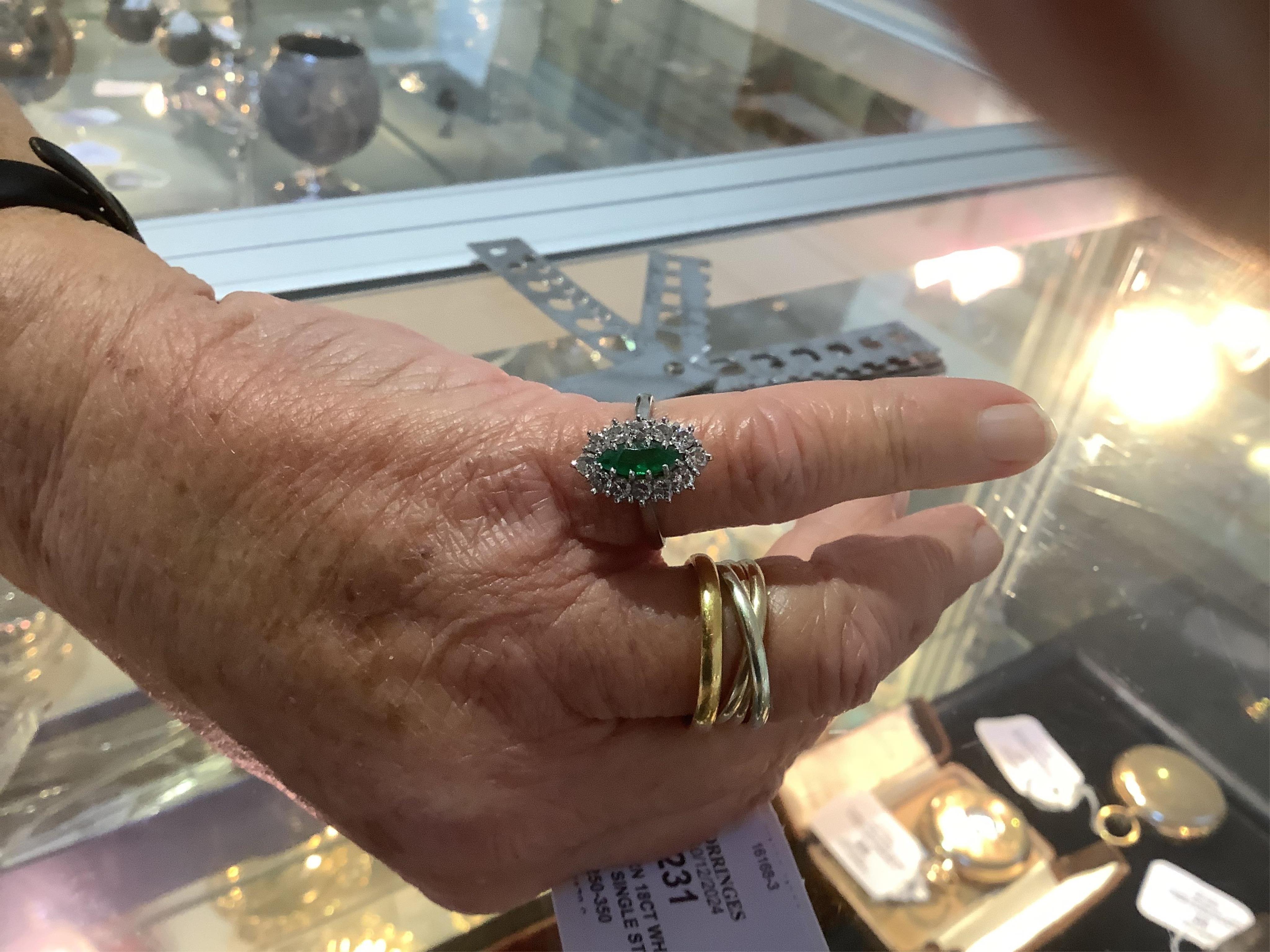 A modern 18ct white gold and single stone marquise cut emerald set ring, bordered with round brilliant cut diamonds